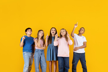Fototapeta premium Preteen children looking up and pointing on yellow background, expressing curiosity and imagination. Education, creativity, learning, and future thinking concept