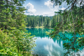Lake Carezza reflecting coniferous forest in the Dolomites, Italy