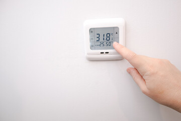 Hand adjusting temperature on a digital wall thermostat for underfloor heating.