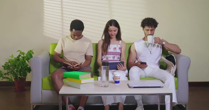 Indian young adult gen z male female girl sitting on couch sofa use tab look screen do new e learning study work indoor place happy teen man read book hold cup drink coffee talk enjoy day spend time