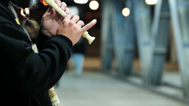 Musician playing recorder outdoors, busking at night on urban street