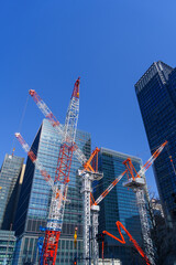Modern construction cranes against a bright blue sky in a business district.