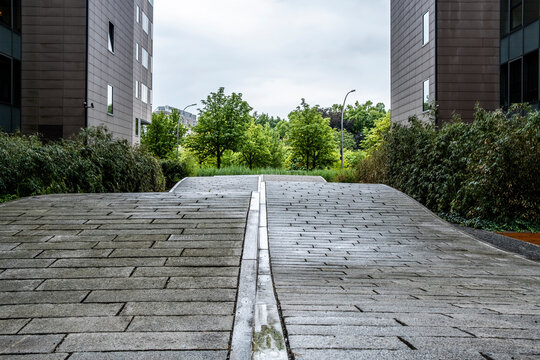 Wet pavement walkway with central drainage and strong perspective between modern buildings showing industrial way route toward future destination