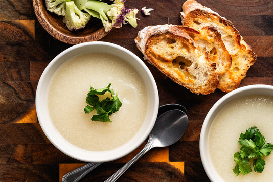 Cauliflower cream soup with grilled bread and cilantro on rustic wooden background