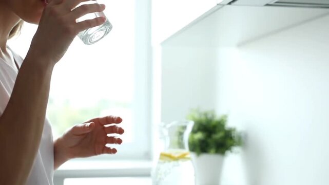 Young woman enjoys a refreshing glass of water in her bright kitchen, prioritizing daily hydration and a healthy lifestyle for overall well-being and vitality