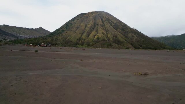 Wide aerial perspective highlights Mount Batok volcanic mountain showing ash fields, sculpted slopes, sparse greenery and raw mountain terrain within East Java natural environment