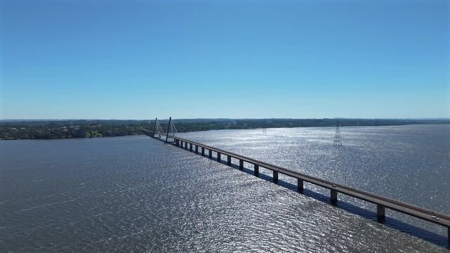 Aerial panoramic pullback establishing Puente Internacional San Roque Gonzalez spanning wide river under clear blue sky