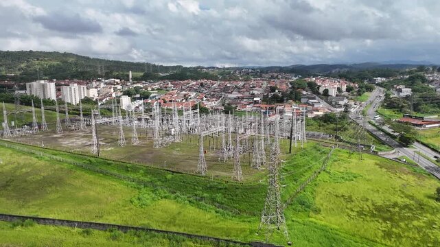 Vis&atilde;o a&eacute;rea de torres de transmiss&atilde;o de energia el&eacute;trica com cabos de alta tens&atilde;o atravessando &aacute;rea urbana e campos abertos, evidenciando a infraestrutura energ&eacute;tica.