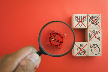 Stop smoking and health risk warning concept. Magnifying glass zooming on cigarette ban sign with destroyed organs symbols. Metaphor of lung cancer, heart disease, stroke, and toxic addiction.