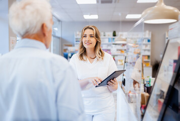 Obraz premium Female pharmacist helps a senior man choose medication in pharmacy.