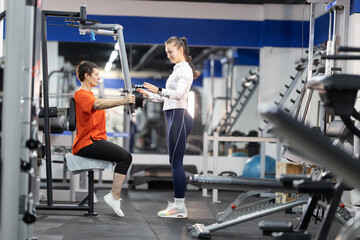 Personal trainer guiding senior woman during chest press workout