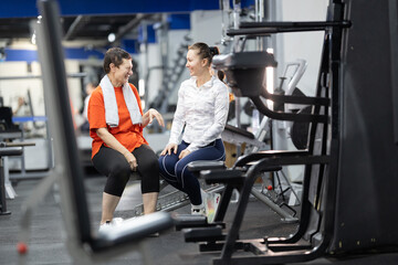 Fototapeta premium Senior woman and coach discussing exercise in gym