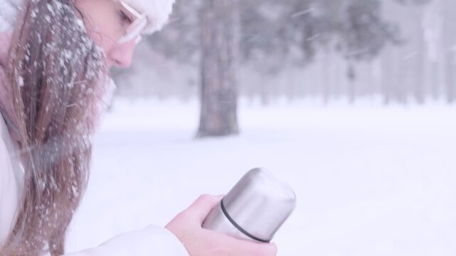 Woman winter tea. Female pouring hot drink from thermos outdoors. Cozy lifestyle concept.