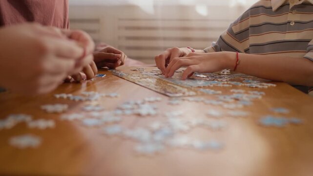 Cropped shot of hands of unrecognizable diverse kids assembling puzzle pieces while sitting at table at home