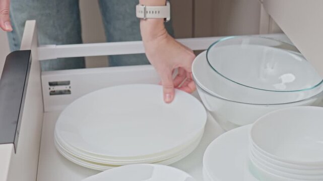 Hand pulling out kitchen drawer with neatly stacked plates and bowls. Concept of kitchen organization and home storage