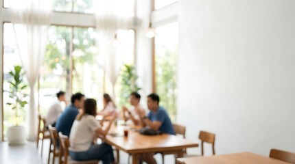 Obraz premium A blurred photograph captures diverse individuals conversing around a wooden table in a modern, bright cafe, suggesting a relaxed informal meeting.