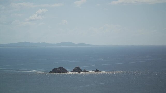 Closer view of Julian Rocks surrounded by ocean water with visible surface movement and distant landforms on the horizon, Byron Bay, Australia.