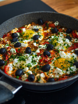 Shakshuka - fried eggs with vegetables and black olives in frying pan on electric stove