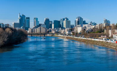 Obraz premium Courbevoie, France - 02 04 2026: Panoramic view of La Defense towers business district, La Seine river and residential housing from Courbevoie Bridge