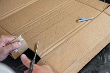 Close-up of hands working on a cardboard prototype at a desk. Startup project concept, product development, prototyping process, creativity, and innovation. Hands-on work, no face visible.