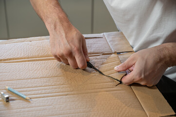 Close-up of hands working on a cardboard prototype at a desk. Startup project concept, product development, prototyping process, creativity, and innovation. Hands-on work, no face visible.