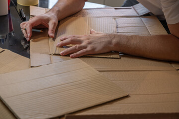 Close-up of hands working on a cardboard prototype at a desk. Startup project concept, product development, prototyping process, creativity, and innovation. Hands-on work, no face visible.
