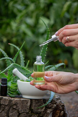 Female hand holding a serum bottle against aloe vera plant and mortar background
