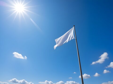 A white flag waving gently on a pole against a blue sky with clouds and sunshine from a low angle view