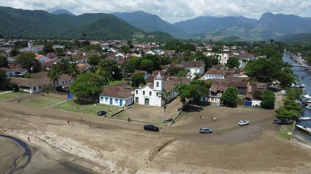 Drone flying from the square in front of Igreja Nossa Senhora das Dores, slowly revealing Paraty, the beach by the river and the mountains with the Atlantic forest that surrounds this historical city
