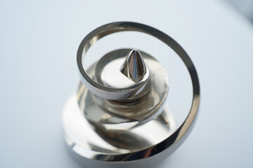 A sleek, modern metallic spiral sculpture with a pointed top, reflecting light and creating an elegant, abstract art piece