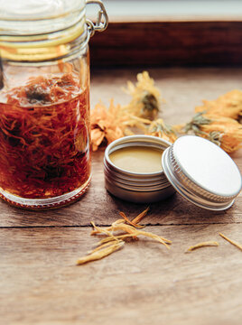 Making homemade Calendula officinalis common marigold cold infusion oil in glass jar and handmade medicinal salve in metal jar. Dry flowers are soaked in olive oil at room temperature. 