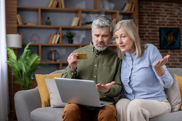 Senior couple on sofa frustrated and worried as they try to complete an online credit card payment...