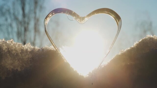 Vertical video (portrait, 9:16) showing a heart-shaped frozen soap form on snow, backlit by the sun in subzero winter conditions. valentine's day