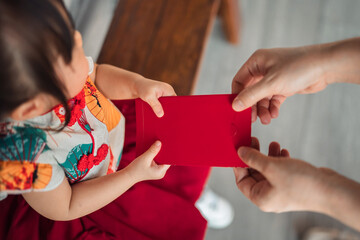 Top view Close-up of adult hands giving a red envelope (Angpao) to a little girl in traditional Chinese dress. Lunar New Year celebration cultural tradition and family blessing concept.