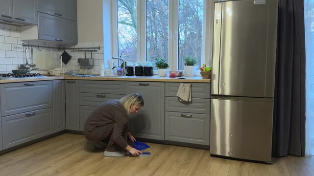 Woman sweeping crumbs from floor into dustpan. Everyday kitchen cleaning routine symbolizing order and household care.