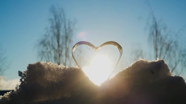 Winter video of a transparent heart-shaped soap filament frozen on snow, glowing with sunlight and creating an abstract symbol of cold, love, and nature. valentine's day