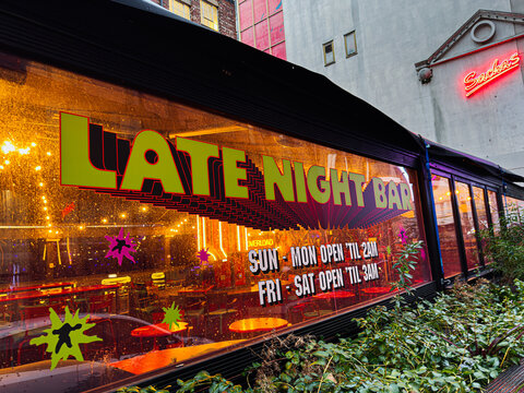 Late Night Bar in Manchester with neon signage and colorful glow along glass storefront. Britannia Sachas.
