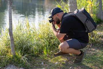 Man Taking Photos in a Public Park. Photographer Capturing Moments in Urban Park. Male Photographer Using Camera Outdoors in Park. Man with Camera Photographing Nature in Park.