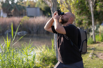 Man Taking Photos in a Public Park. Photographer Capturing Moments in Urban Park. Male Photographer Using Camera Outdoors in Park. Man with Camera Photographing Nature in Park.