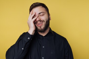 Obraz premium Man smiles and covers his face with hand against a yellow background while expressing a moment of joy