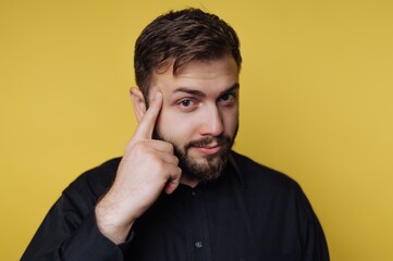 Obraz premium Man with beard thinks while touching his temple against a bright yellow background in a studio setting
