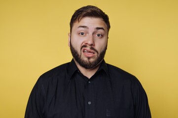 Obraz premium Man makes a funny face on a yellow background while wearing a black shirt and looking at the camera