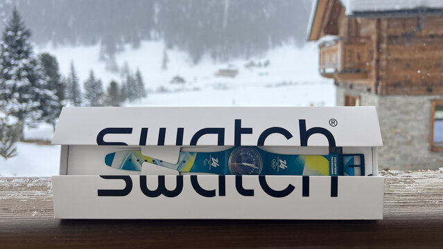 Livigno, Italy - February 3, 2026: Swatch volunteer wristwatch in original packaging displayed on a wooden terrace in Livigno, featuring Milano Cortina 2026 Winter Olympics branding