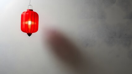 A red lantern hanging from a white ceiling with a shadow on the wall