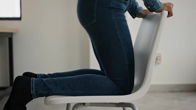 Seated motion from side view. Close-up side profile of a person sitting down on a simple chair, emphasizing balance and weight shift.