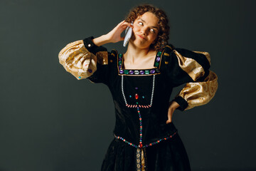 Fototapeta premium Portrait of a young aristocratic woman talking on mobile phone dressed in a medieval dress on dark background