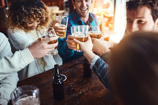 Friends, cheers and restaurant with fun celebration and reunion with beer at a pub or bar with happy people. Group, glasses and smile with drinks toast for event or birthday together with laugh