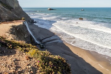 Clifftop view of waterfall meeting Pacific Ocean shoreline © Thomas