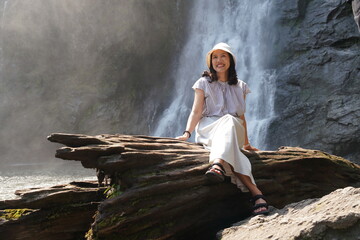 Obraz premium An Asian female backpacker tourist sits by a waterfall, relaxing and enjoying her summer vacation. ส่งความคิดเห็น