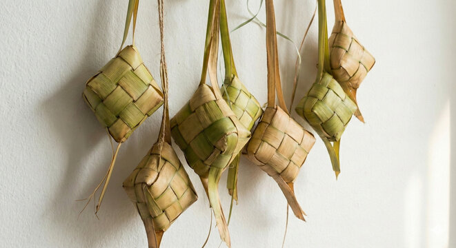 landscape photo of traditional Indonesian Ketupat hanging against a white wall, ideal for festive Eid al-Fitr editorial content or culinary blog headers
